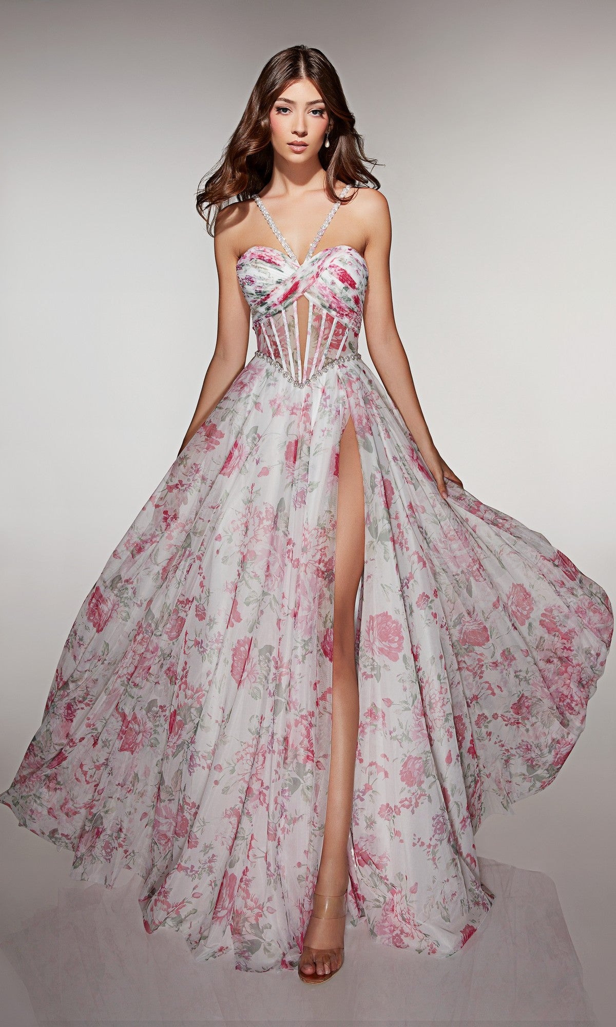 A woman stands against a plain background wearing the Long Prom Dress: Alyce 61994, featuring a sheer floral design, corset bodice, spaghetti straps, and high leg slit.
